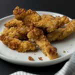 pile of chicken tenders on a white plate against a black background