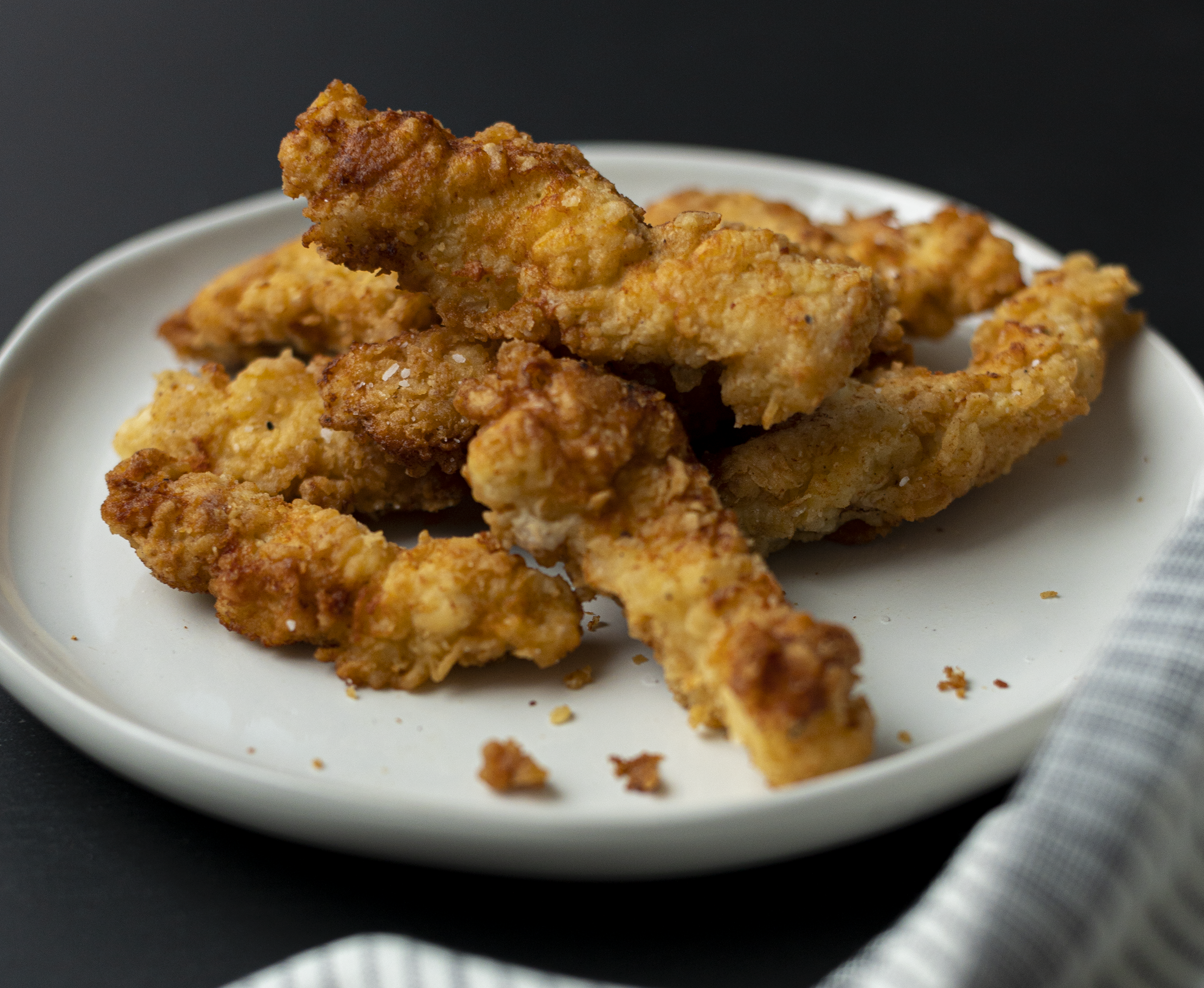 pile of chicken tenders on a white plate against a black background